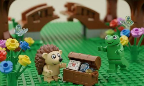 Pic, un mic arici din cărămizi LEGO, pare mândru și uimit în timp ce deschide cu lăbuțele un cufăr mic de lemn; lângă el, Blip, o broască verde LEGO, zâmbește fericit și pare că aplaudă; într-o poiană colorată cu plăci verzi, flori multicolore și fluturi translucizi, în fundal un pod brun puțin rupt și copaci cu trunchi texturat și frunziș rotund, iar în cufăr se văd pietre translucide sclipitoare și o scrisoare pliată din „hârtie” LEGO — scenă caldă, curioasă și prietenoasă, cu lumină blândă și culori vii.